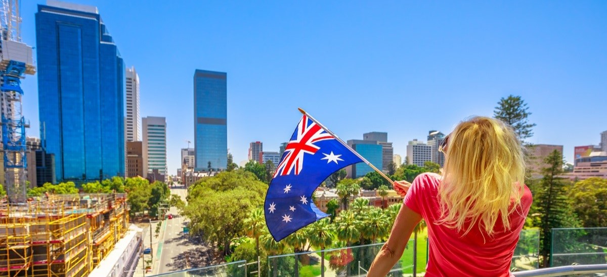 woman with back to camera looking out at Australian city waving an Australian flag