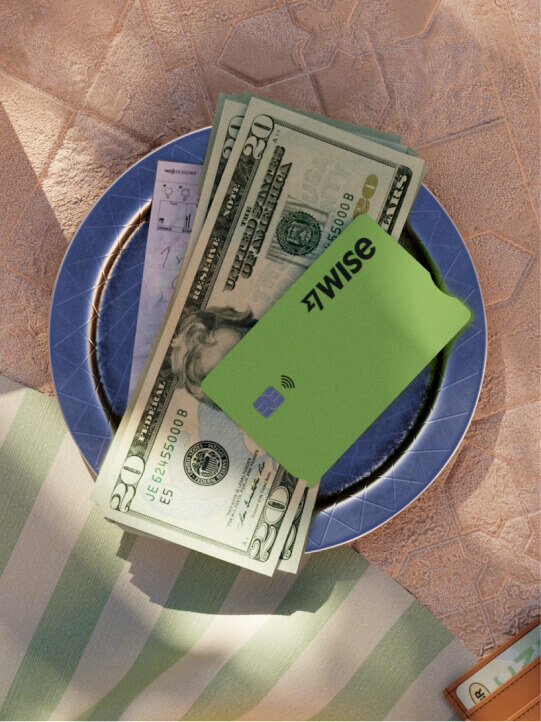 Une assiette repose sur une table. Sur cette assiette, il y a des USD et une carte Wise.